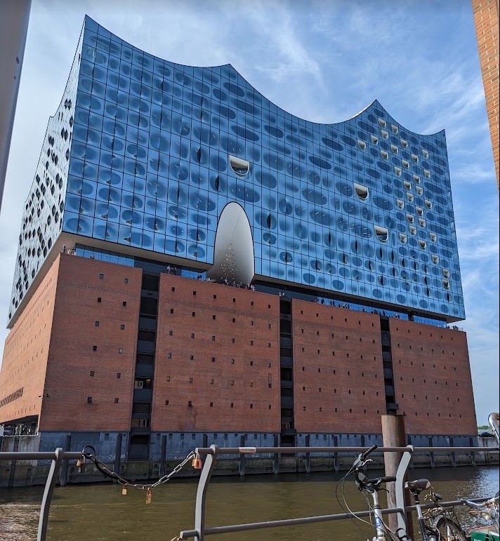 Blue glass structure with inverse scalloped roof sits atop red bricks