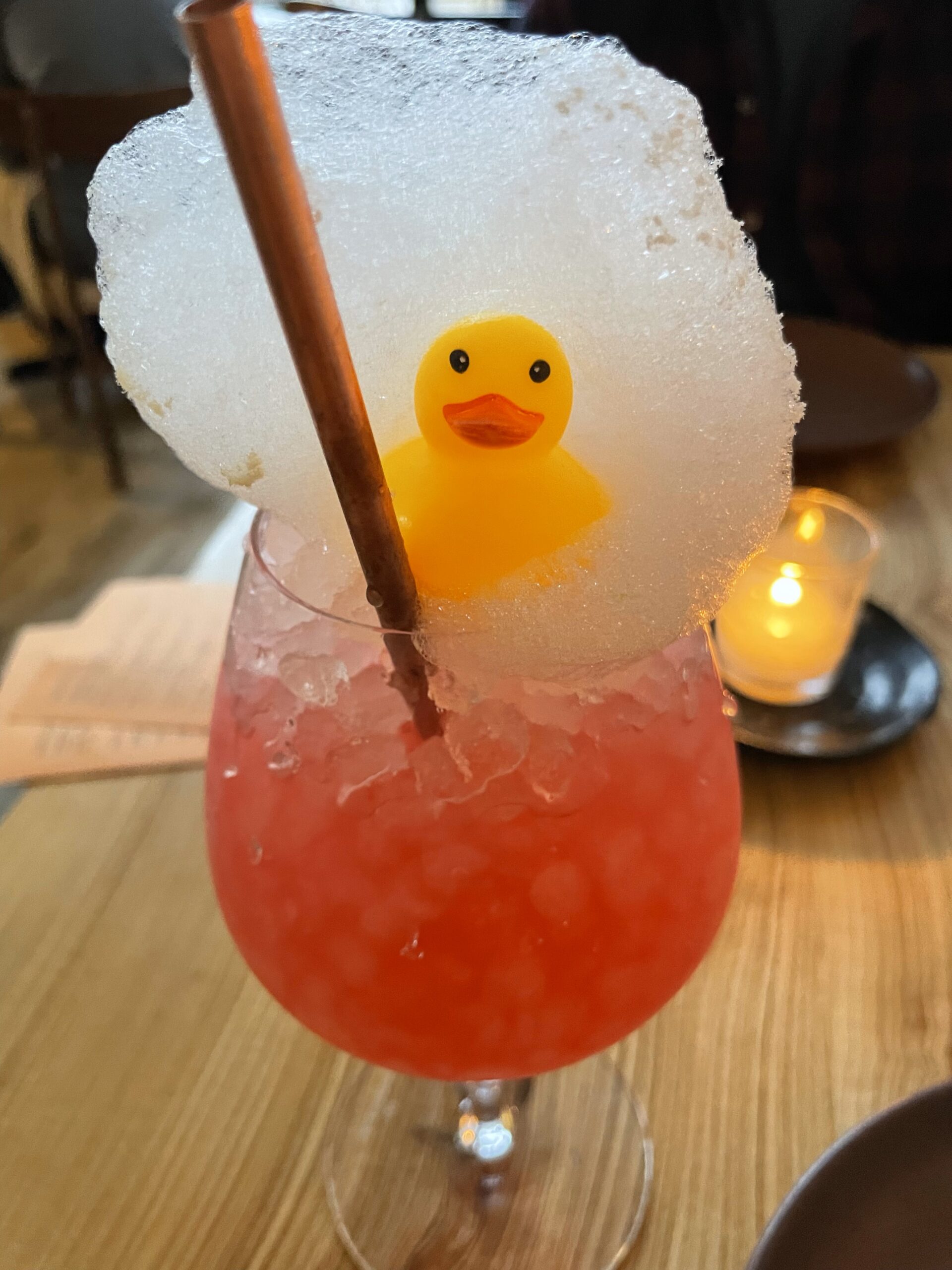 Pink drink in a wine glass with rubber ducky, foam, and straw sit on top