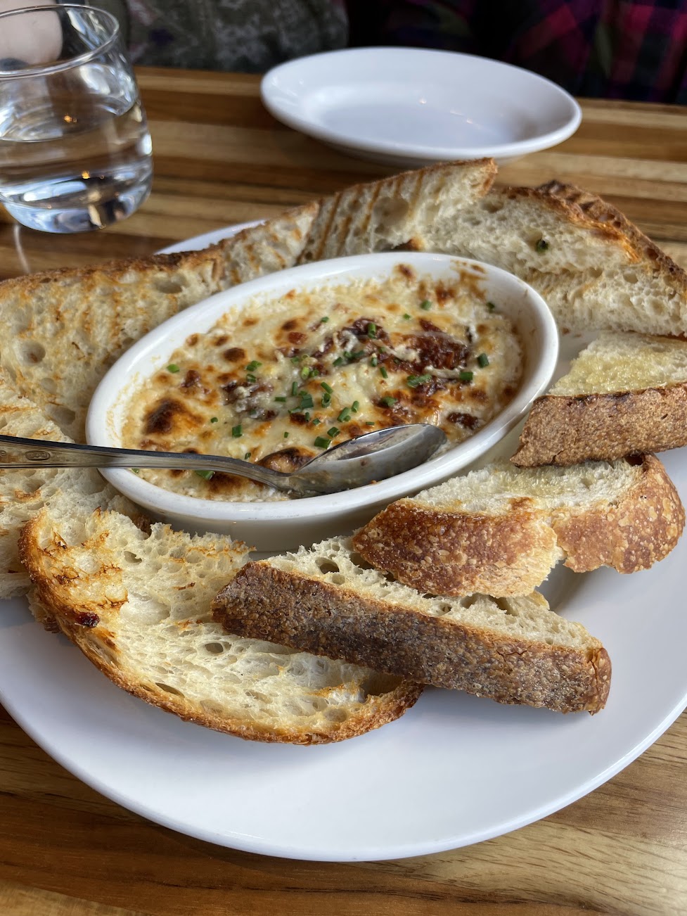 Melted spinach artichoke dip in white dish surrounded by slices of toasted bread on a white plate