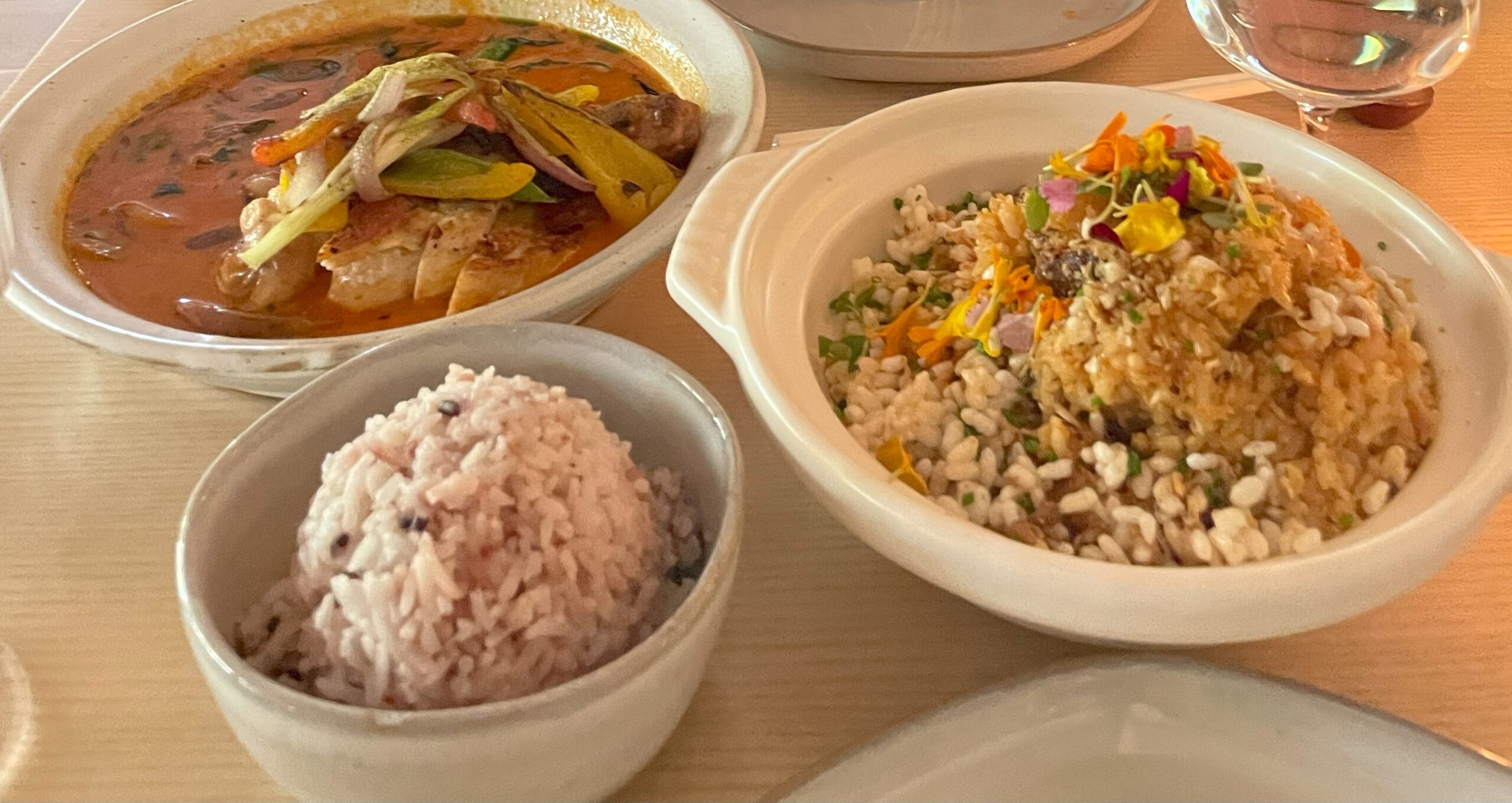 Three bowls sit on beige table. small bowl with rice on bottom left, top left has brown curry, right larger bowl has fried rice