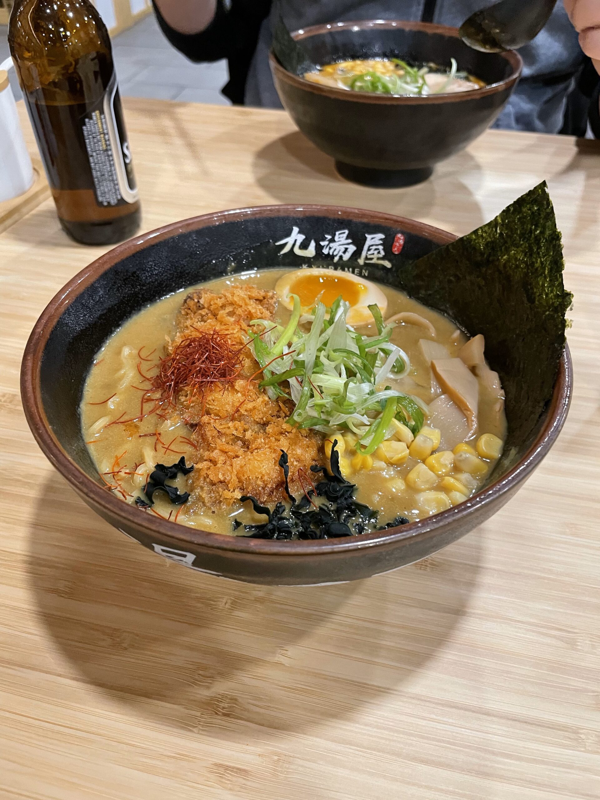 Ramen noodles with boiled egg, shaved onions, seaweed, saffron, and tonkatsu in a black ceramic bowl